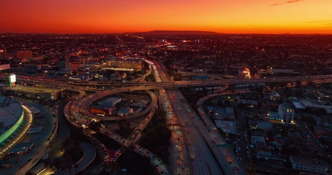 Amazing orange sky over the vast panorama of Los Angeles, California, USA at sunset. Multiple cars run by the highways and interchange across the city. Aerial view.