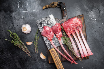 Fresh uncooked lamb chops and ribs with thyme on cutting board dark textured background overhead meat preparation