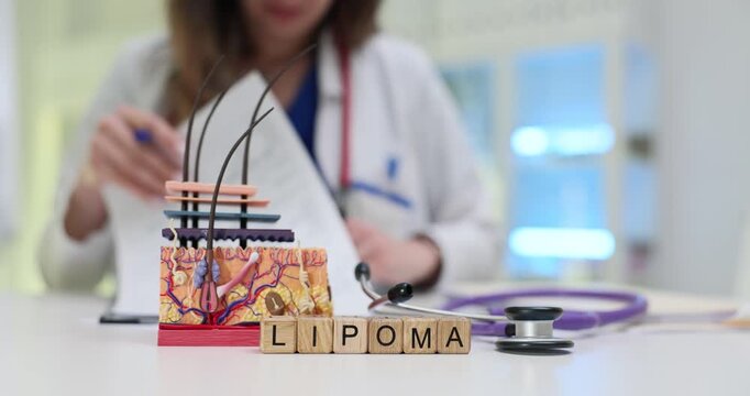 Word Lipoma of wooden cubes and skin layer anatomical model in doctor office. Female dermatologist reads patient records before appointment in clinic
