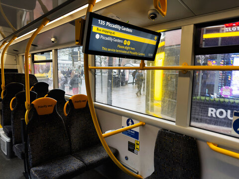 Inside Manchester city bus with priority seating and a digital route display overlooking a rainy street