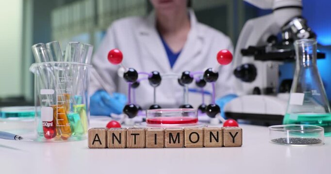 Laboratory worker carefully records observations in laboratory journal. Wooden letter cubes form word Antimony identifying substance under analysis