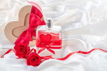 HOLIDAY BACKGROUND with A heart-shaped gift box made of kraft cardboard with a perfume bottle, a heart AND  RED ROSES