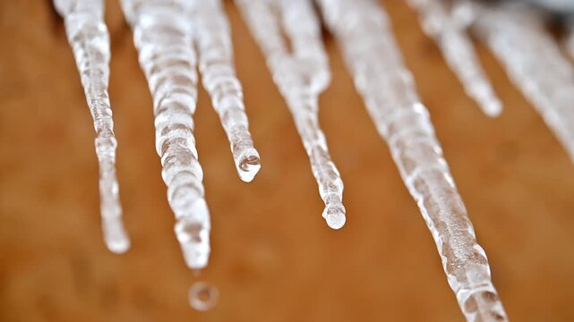 A close up of icicles hanging from a brown surface. The icicles are long and thin, and they are all different sizes. Scene is serene and peaceful, as the icicles seem to be suspended in midair