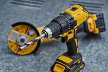Close-up of a cordless drill with a metal drill bit and an angle grinder on a steel surface. Concept of construction, workshop tools, industrial work, maintenance and professional craftsmanship.