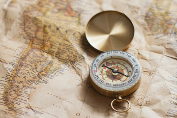 Golden compass lies on an antique world map showing South America. This aesthetic scene represents navigation, historical exploration, business strategy planning and the spirit of wanderlust.