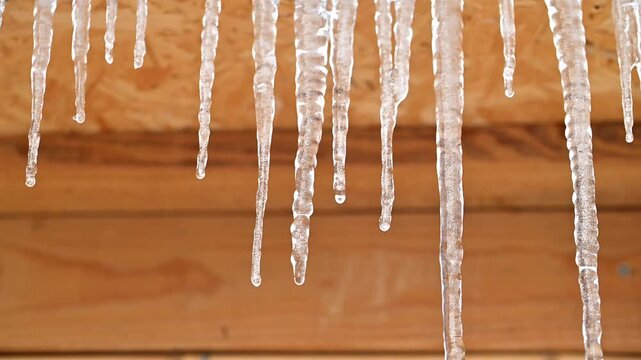 A row of icicles hanging from a roof. The icicles are clear and shiny, and they are all different sizes. The scene is peaceful and serene, with the icicles glistening in the sunlight
