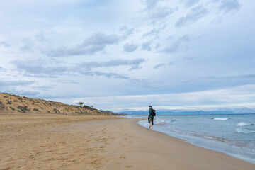 Naklejka premium A man walks along the beach near Guardamar del Segura, Alicante, Spain, with eroded dunes, fallen twisted trees, and exposed roots reflected in shallow water, part of Parque Alfonso XIII