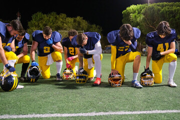 American football players kneeling on the field, showing unity, prayer, or protest