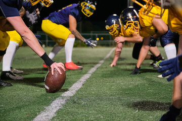American football players lining up at the scrimmage line, gripping the ball before a play