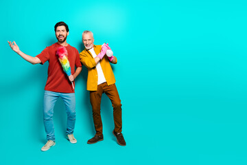 Fototapeta premium Two men posing with cleaning tools smiling together against a teal studio background for family friends lifestyle