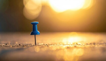 A solitary blue pushpin standing upright in a sunlit, textured environment with soft bokeh highlights.