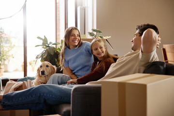 Family relaxing together at new home with dog and moving boxes