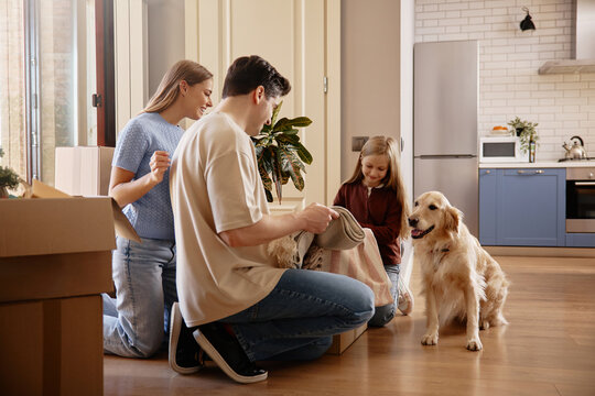 Family unpacking boxes with golden retriever in new kitchen