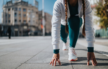 Urban athlete crouches in starting pose on a bright city street, ready to run.