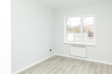 Fototapeta premium Empty interior room after renovations with gray freshly painted walls and big window, allowing natural light, with a wooden floor, a radiator beneath the windows