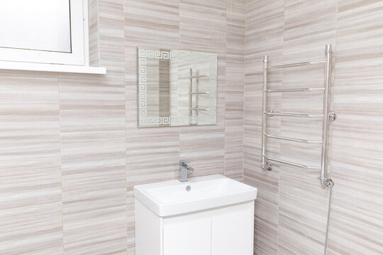 Modern bathroom interior featuring a white sink, mirror, and towel warmer against light-colored tiled walls with a window providing natural light