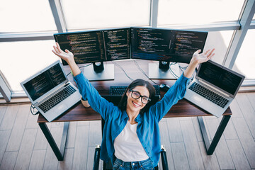 Female programmer works at a multi screen setup with laptops and monitors in a modern office