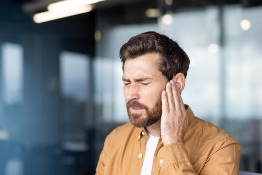 Man clutching his ear in pain, showing severe earache and discomfort from infection, tinnitus or hearing loss stressed, tired, and seeking medical help for relief