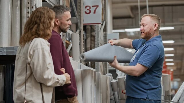 Low angle shot of male shop assistant showing roll of grey wallpaper while married couple looking at it and discussing