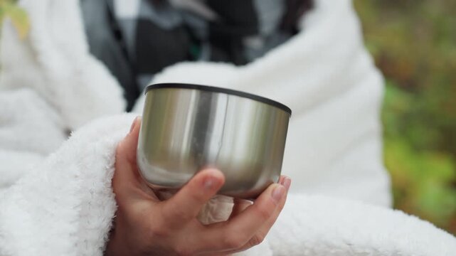 Warm hands present, Gentle hands hold empty vessel softly, Hands wrapped in fleece cradle vacant cup gently, Softly wrapped hands with fleece hold empty cup amidst blurred foliage background