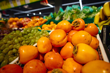 Fresh persimmons among various fruits in a grocery store produce section during daytime