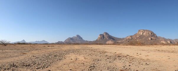 Wide empty desert landscape with rocky plateaus and distant rugged mountains beneath a clear blue sky, ideal for minimal natural backgrounds, climate awareness visuals, and vast open environment