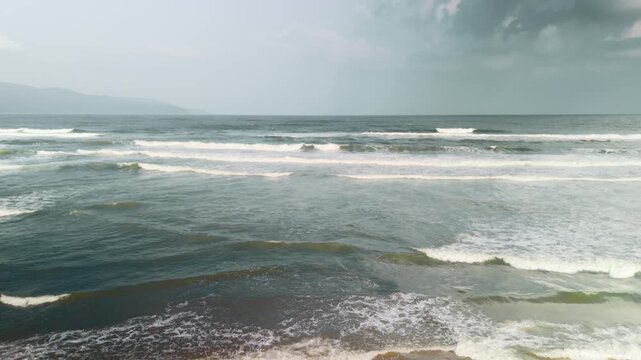 Ocean waves breaking on the shore of my khe beach in da nang, vietnam, extending towards the horizon under a cloudy sky, depicting a vast and serene coastal environment