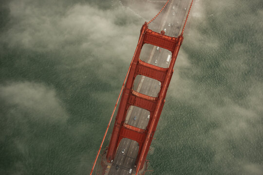 Aerial view of the iconic Golden Gate Bridge piercing through a sea of fog, its vermillion towers contrasting with the muted tones of the water, San Francisco, California, United States.