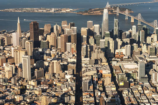 Aerial view of skyscrapers casting long shadows, the iconic Bay Bridge stretching across the water to Yerba Buena Island, San Francisco, California, United States.