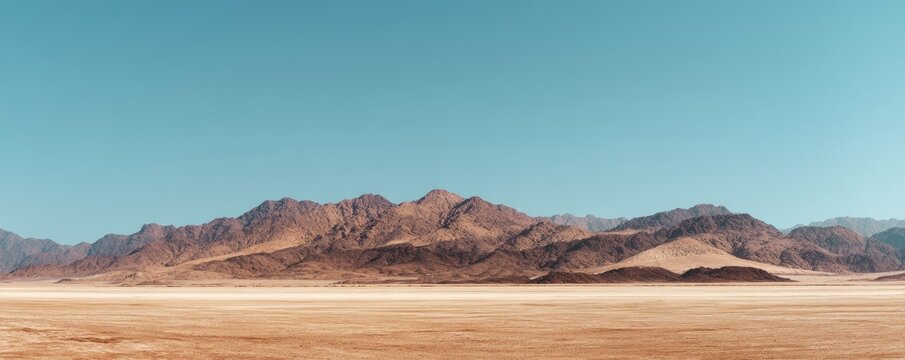 Wide empty desert plain with distant rocky mountain range under a clear blue sky creating vast open space and minimal natural scenery for climate and environmental concepts