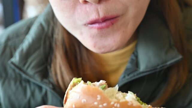 Footage of young Asian woman while eating a hamburger in cafe. A hamburger is a sandwich consisting of a cooked meat patty on a bun or roll.