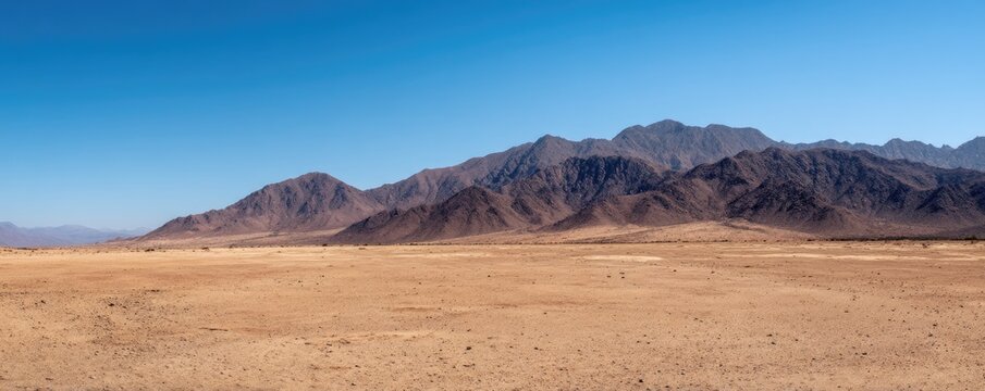 Wide empty desert plain with distant rugged mountain range and clear blue sky creating vast open space and minimal natural scenery for climate environment and background concepts