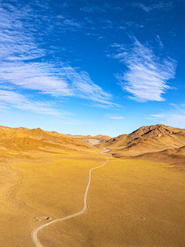 Aerial view of a winding road cuts through the arid landscape, where the ochre earth meets the azure sky, creating a stark yet beautiful contrast, Puna, Argentina.