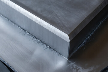 Close-up of a precisely cut, thick metal slab with sharp, beveled edges and a brushed metallic surface, conveying strength and industrial material.
