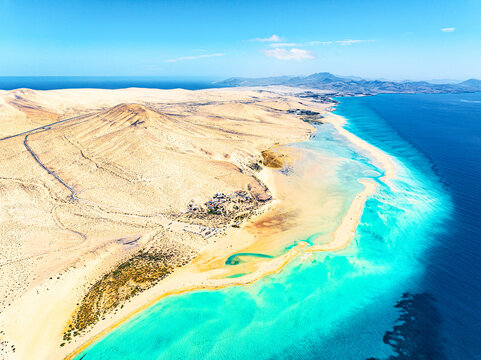 Aerial view of turquoise waters meeting the golden sands, creating a stunning contrast against the clear blue sky, Parco natural de Jandia, Costa Calma, Fuerteventura, Canary Islands, Spain.