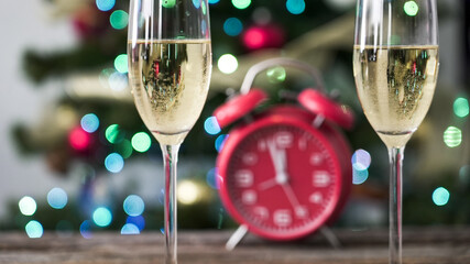 Celebration with champagne glasses in front of a Christmas tree and a red alarm clock showing midnight