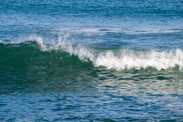 Naklejka premium a cresting ocean wave breaking into white foam as it rolls across the blue sea surface.