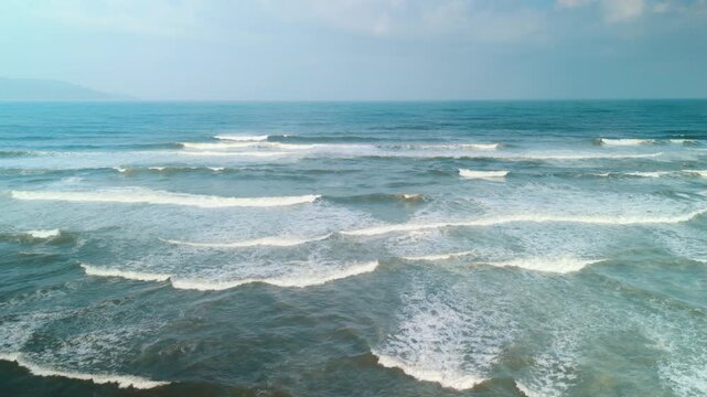 Waves rolling toward da nang's coast form white foam patterns on deep blue water under a bright, clear sky, a tranquil tropical seascape with distant horizon and sunlight