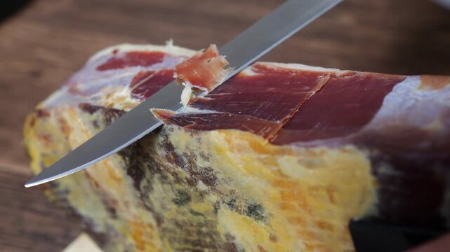 Expertly slicing thin, savory spanish serrano ham from a whole leg with a long knife, showcasing artisan carving technique for gourmet charcuterie and authentic tapas preparation