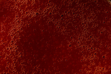 Abstract macro shot of red liquid with bubbles, ideal for background or design.