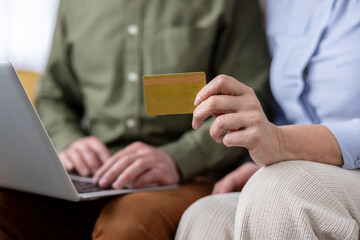 Couple sits at home browsing on a laptop while one hand holds a credit card, preparing an online purchase to illustrate e-commerce, digital payment and secure internet banking