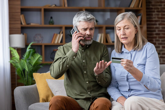 Mature couple feeling stressed and worried while dealing with a scam or financial fraud, with the man speaking on the phone and the woman holding a credit card