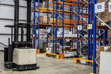 Narrow track pallet forklift truck positioned in front of warehouse racking, with storage shelves and pallets visible in the background. © Val