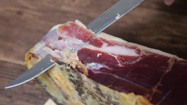 Expertly slicing a thin piece of premium serrano ham from a whole leg, revealing the intricate marbling and aged texture of the gourmet dry cured meat, ready for a delicious tasting experience