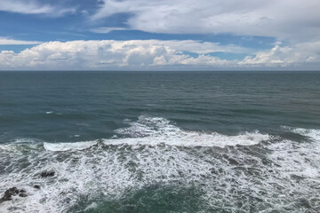 Fototapeta premium High Angle Seascape View Capturing the White Foamy Waves Crashing in the Foreground and the Endless Ocean Horizon. The Blue Sky is Filled With Dynamic Clouds, Creating a Scenic Marine Environment.