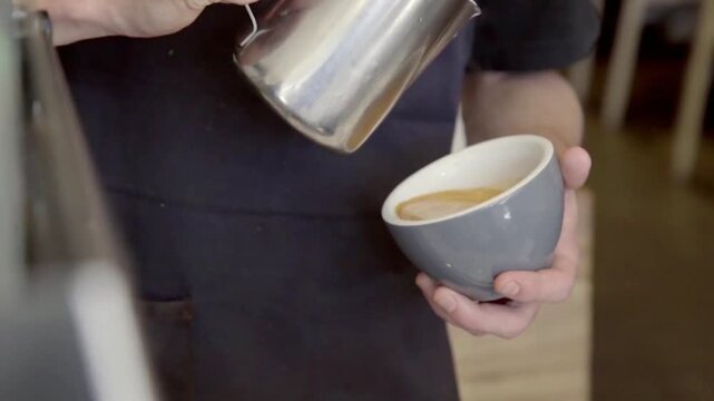 Close up of professional barista pouring milk to create Rosetta latte art in a grey cup