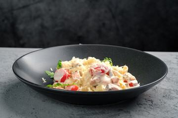 Creamy fettuccine pasta with tender salmon pieces, cherry tomatoes, parmesan shavings and fresh arugula garnish in black bowl. Gourmet Italian seafood pasta