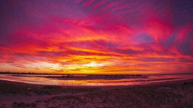 Timelapse: Djerba island beach at sunset, dramatic sky reflected on calm water, wide coastal landscape, vibrant clouds, tranquil atmosphere, nature, travel destination, Mediterranean Sea, Tunisia