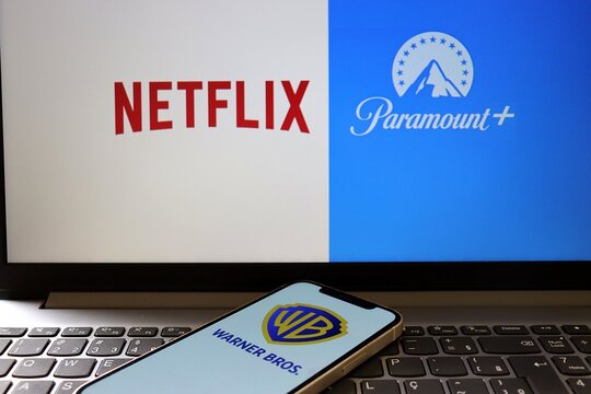 Warner Bros. logo on a smartphone screen with Netflix and Paramount logos in the background. Netflix, Paramount and Warner Bros.
