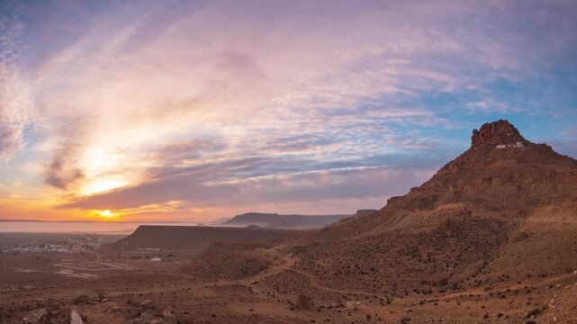 Timelapse: Ksar Guermassa hilltop berber village at sunrise, rocky desert landscape dramatic sky, ancient architecture, arid terrain, heritage, history, travel destination, Tataouine, Tunisia